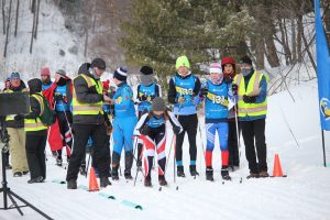 A Nordic ski racer crouches at the beginning of his race with several other racers lined up and behind him at the UP Nordic Ski Center in February 2022.